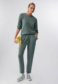 Sweat-shirt vert à manches longues avec détail brodé, associé à un pantalon fuselé assorti et des baskets métalliques. Accent de sac jaune.