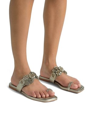 Sandali piatti con finitura metallica argento, caratterizzati da accenti floreali decorativi con gemme. Design open-toe e suola squadrata.