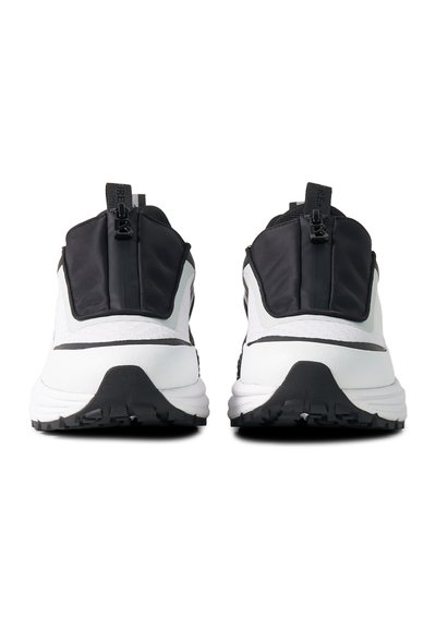 Paire de chaussures de sport blanches et noires vues de dos, avec languettes de talon noires munies de tirettes de fermeture éclair et semelles noires texturées.