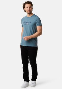 Jasnoniebieska bawełniana koszulka z krótkim rękawem z nadrukiem "Nadmorskie". Połączona z czarnymi dżinsami i białymi sneakersami.