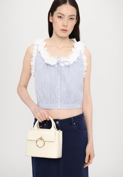 Blauw en wit geruite crop top met een rimpelende kanten kraag; model houdt een kleine witte handtas vast met een ronde gouden ringaccent.
