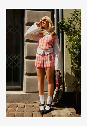 Ensemble de top court à carreaux rouges et blancs avec un haut blanc en dessous. Des ballerines noires à bouts pointus avec détail de boucle. Les accessoires incluent des lunettes de soleil rouges et un sac à main.