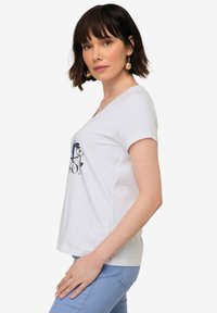 Camiseta blanca de manga corta con escote en V y un diseño gráfico en negro y azul en la parte delantera. Material de algodón suave, corte relajado.