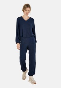 Marineblaues Loungewear-Set mit einem V-Ausschnitt-Pullover und Hose mit elastischem Bund, ausgestattet mit einem strukturierten Stoff und Seitentaschen.