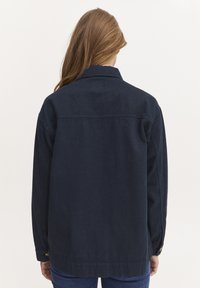 Marineblå denimjakke med krage, lange ermer og matchende knapper. Har rett kant og teksturert stoff.