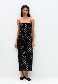 Musta pilkullinen midi-mekko, jossa on ohuet olkaimet, muotoileva siluetti ja hienovarainen rypytys. Sileä kangas, jossa on kevyt kiilto. Yhdistetty mustiin flats-kenkiin.