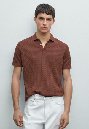 Brown ribbed short-sleeve polo shirt with a textured pattern and three-button placket, paired with white pants, worn against a light backdrop.