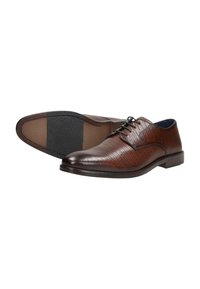 Braune Lederschuhe mit strukturierter Oberfläche, flachen Schnürsenkeln, abgerundetem Zehenbereich und einer kontrastierenden schwarzen Gummisohle.