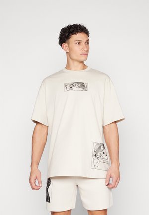 Beige cotton t-shirt with oversized fit, featuring two black and white graphic prints on the front. Short sleeves and crew neck design.