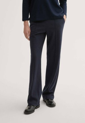 Pantaloni tailored blu navy realizzati in tessuto strutturato, con un design a gamba dritta e tasche laterali, abbinati a scarpe nere.