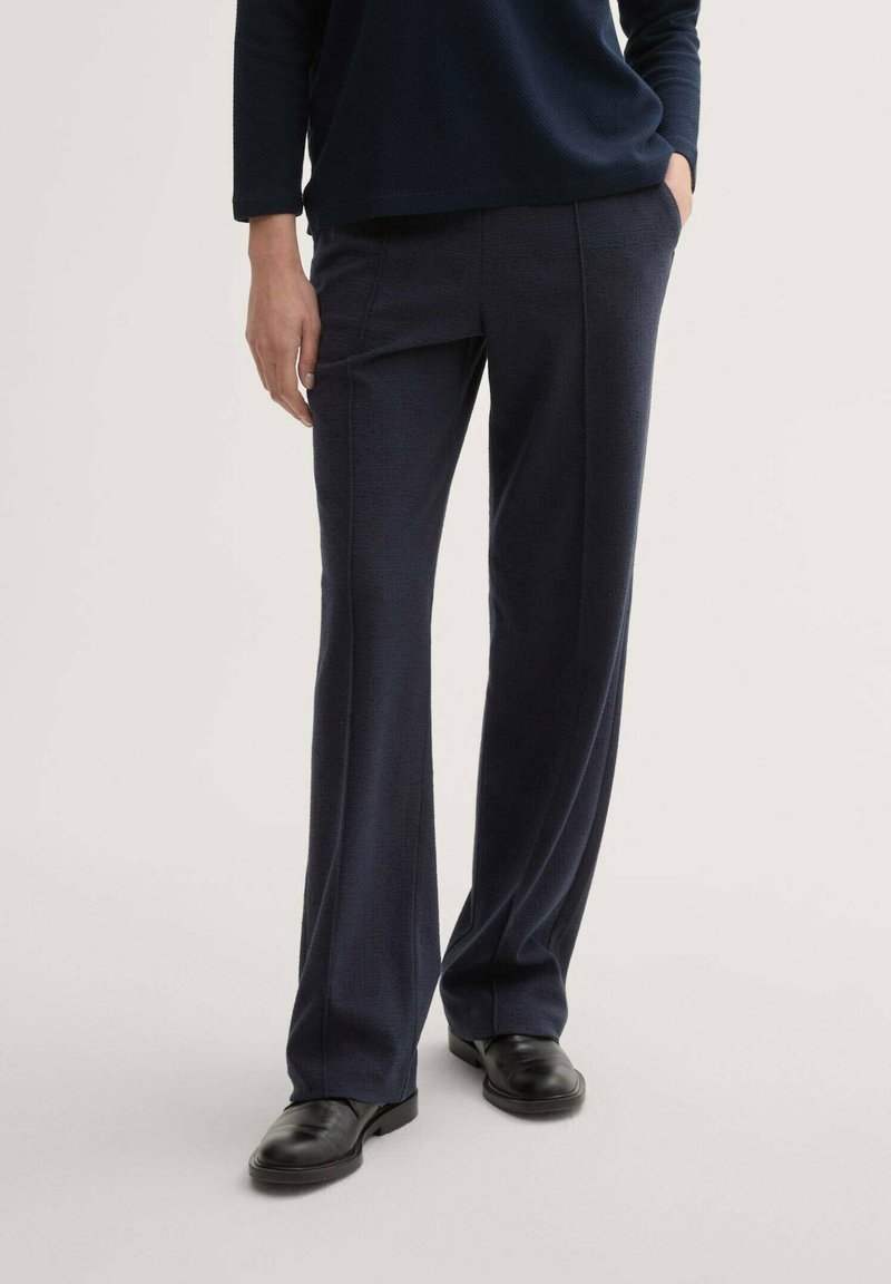 Pantaloni tailored blu navy realizzati in tessuto strutturato, con un design a gamba dritta e tasche laterali, abbinati a scarpe nere.