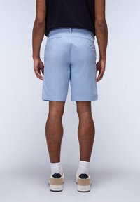 Shorts bleu clair avec une coupe classique, deux poches arrière et une texture lisse, associés à des baskets beiges et des chaussettes blanches.