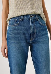 Denimjeans in Mittelblau mit einer verwaschenen Optik, klassischem Five-Pocket-Design, Gürtelschlaufen und metallener Knopfverschluss.