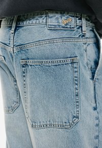 Hellblaue Jeans mit hoher Taille, ausgeprägten Gesäßtaschen und goldenen Logo-Details am Bund.