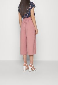 Pink culotte pants with an elastic waistband paired with a floral-patterned navy top. White block-heeled sandals complete the outfit.