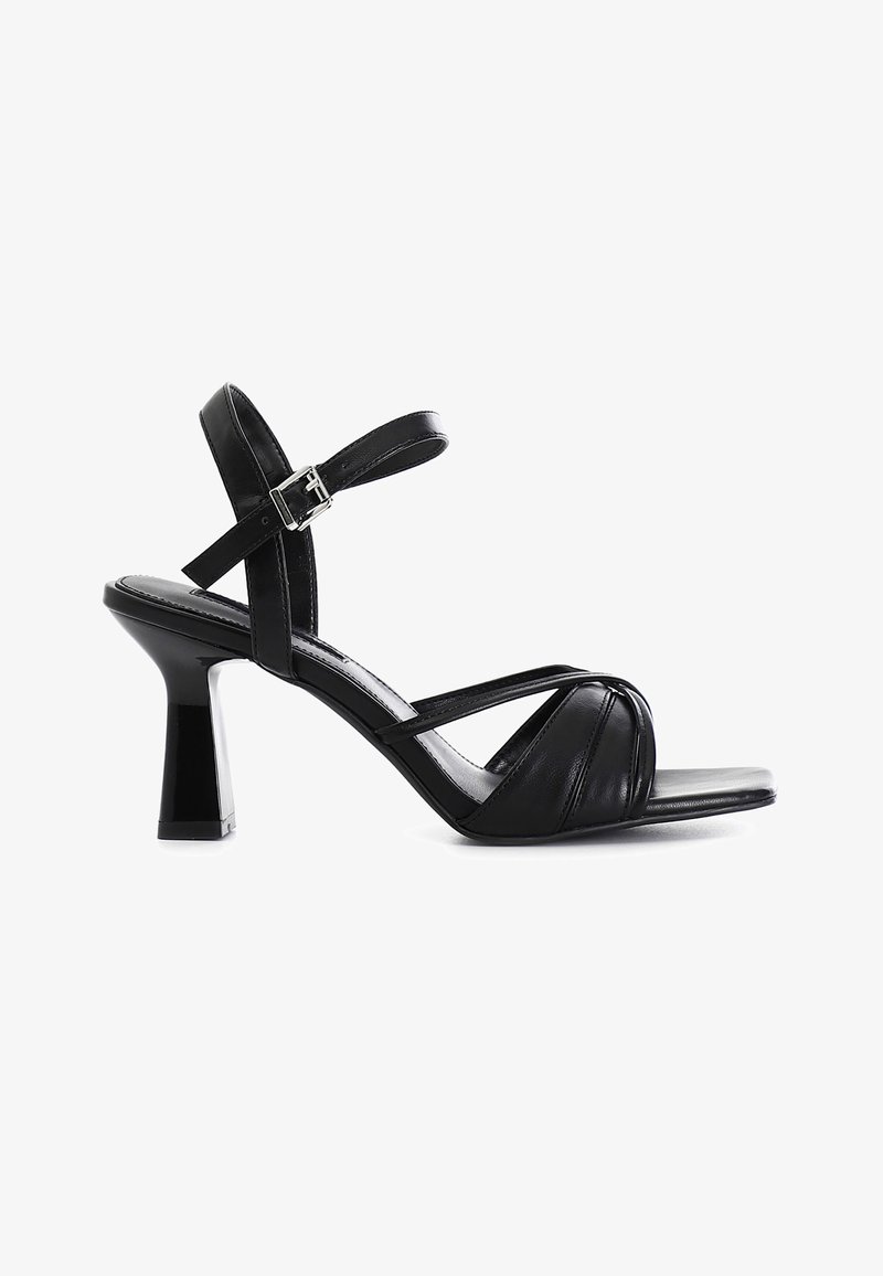 Sandale à talon haut en cuir noir avec des brides croisées à l'avant, une bride à la cheville avec boucle et un bout carré sur fond blanc.