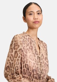 Bluse mit Leopardenmuster aus leichtem Stoff, mit Knopfverschluss, plissiertem Design und elastischem Bund, in sanften Beige- und Brauntönen.