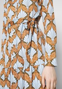 Robe à motif floral en brun, bleu et orange. Elle présente une taille ceinturée, des manches longues et des boutons sur le devant.