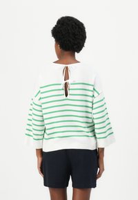Pull en tricot blanc avec des rayures horizontales vertes, doté d'un col rond, de manches larges et d'un dos découpé attaché par un ruban blanc.