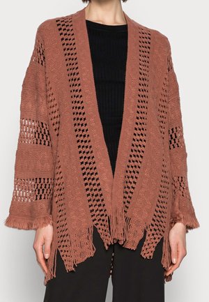 Poncho en tricot ouvert de couleur rouille avec un col en V, des motifs complexes, un ourlet à franges et des manches amples. Matière texturée tout au long.