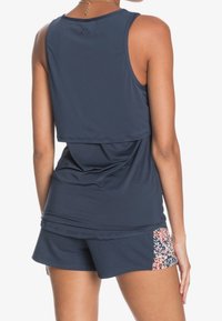 Marinblå sporttopp med lös passform och lagerbak. Tillsammans med matchande shorts med ett blommigt sidopanel.