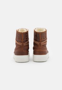 Brown leather ankle boots with white rubber soles. Features a soft interior lining, decorative strap, and embossed logo on the back.
