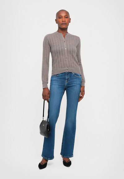 Cardigan a coste grigio chiaro con colletto alto, con bottoni sulla parte anteriore, abbinato a jeans blu svasati e ballerine nere, mentre tiene una piccola borsa nera.