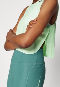 Lichtgroene mouwloze top met geplooide achterkant, gecombineerd met donker groene nauwsluitende legging met een zijzak en doorgestikte details.