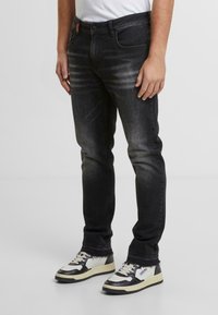 Jeans de denim negro con un diseño ajustado, que presentan un sutil desgastado y costuras en contraste, combinados con zapatillas en blanco y negro.