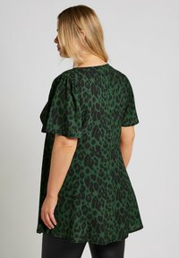 Top verde con stampa leopardata, con maniche a sbuffo corte, vestibilità ampia e scollatura rotonda. Il tessuto appare liscio con una texture leggermente lucida.