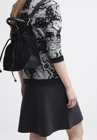 Svart och vit mönstrad sweatshirt, grå utställd kjol och en svart mocka ryggsäck med dragsnöre och en triangelformad läderbotten.