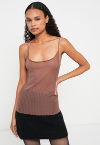 Brun ribbet topp med tynne stropper, med en kontrasterende teksturert bunn. Brukt med et svart, lodden skjørt. Glatt, strikket stoff.