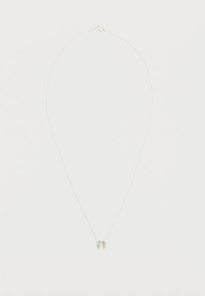 Collier fin en chaîne d'argent avec un petit pendentif minimaliste en forme de fer à cheval sur un fond blanc uni.