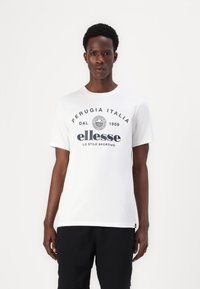 Bílý bavlněný tričko s kulatým výstřihem a krátkými rukávy, s černým písmem, které zahrnuje "Perugia Italia" a branding "ellesse".
