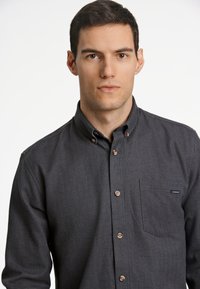 Camicia button-up grigio scuro con un motivo a spina di pesce, colletto rotondo e taschino sul petto, con bottoni marroni e un'etichetta del marchio sulla tasca.