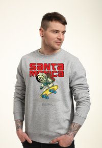 Šedá mikina s barevným grafikou kostlivce astronauta na skateboardu. Text zní "SANTA MONICA" v tučných červených písmenech.