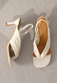 Weiße Leder-Sandalen mit einem gewundenen Oberdesign, quadratischen Zehen und einem schmalen Knöchelriemen. Mit einem bescheidenen Absatz und brauner Innensohle.