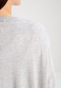 Ljusgrå, mjuk stickad tröja med avslappnad passform, med rundad halsringning och något nedfallna axlar, som visar en subtil textur.