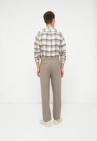 Heren geruite shirt in beige en zwart met lange mouwen en knoopdetails, gecombineerd met lichtgrijze broek en witte sneakers.