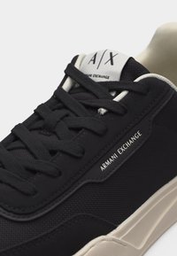 Baskets Armani Exchange noires avec lacets noirs, semelle blanche et logo sur le côté et la languette.