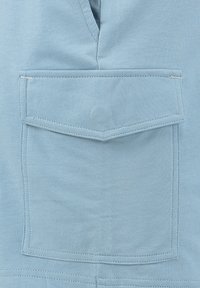 Jasnoniebieska bawełniana tkanina z prostokątną naszywaną kieszenią z okazanym szwem po obrysie. Tekstura jest miękka i gładka.