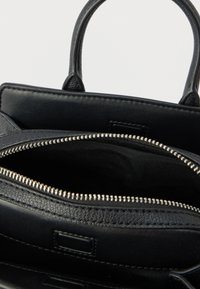 Czarna skórzana torebka z główną przegrodą zamykaną na suwak i dwoma górnymi uchwytami. Wnętrze wyłożone materiałem. Charakterystyczny teksturowany detal na zewnątrz.