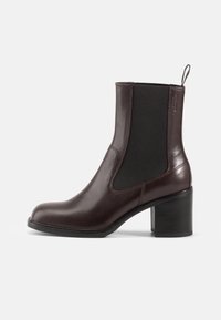 Botas de tornozelo em couro castanho, com painéis laterais elásticos, bico arredondado e salto bloco. Textura suave e detalhe de costura discreta.