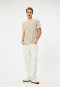 Camiseta corta a rayas en crema con rayas beige, combinada con jeans rectos blanco roto y zapatillas beige. Diseño sencillo, ajuste casual.