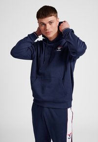 Marineblauwe pullover hoodie met een voorzak, trekkoordcapuchon en geribbelde manchetten. Bevat een logo op de borst en bijpassende joggingbroek.