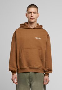 Brun oversized hoodie lavet af bomuldsblanding, med en frontlomme og hvid trykt tekst. Lange ærmer med ribbede manchetter. Casual design.