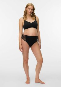 Melnas krūšturis grūtniecēm ar apaļu kakla izgriezumu un vieglu audumu, kombinēts ar melnām augsta vidukļa biksītēm ar mežģīņu sānu akcentiem.