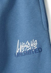 Blå bomullströja med texturerad tyg, broderad vit och marinblå text "Awesome Unlimited" över framsidan. Standard design med rund hals.