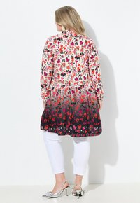 Abito a maniche lunghe con motivo a gradiente di cuori rossi e neri, realizzato in tessuto bianco, e dettagli a peplo. Abbinato a pantaloni bianchi aderenti e tacchi argento.