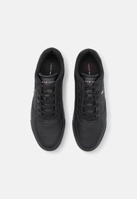 Baskets en cuir noir avec un design à lacets, des détails perforés sur le bout, et une languette et un accent sur le côté de marque en rouge et blanc.